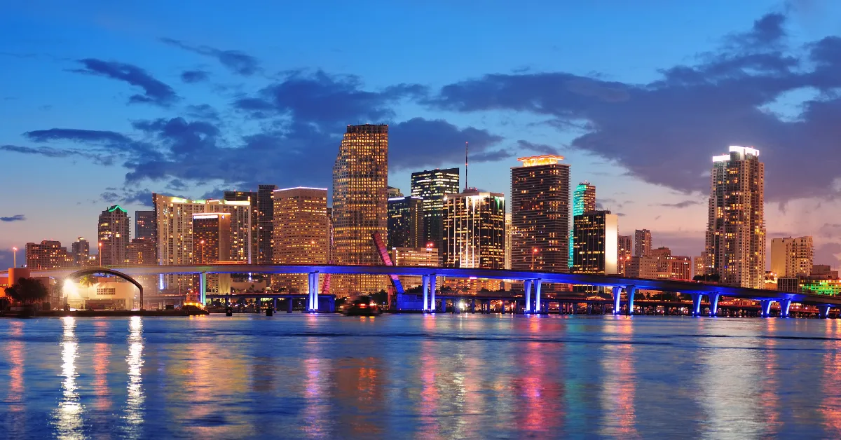 Miami city skyline panorama at dusk with urban skyscrapers and bridge over sea with reflection